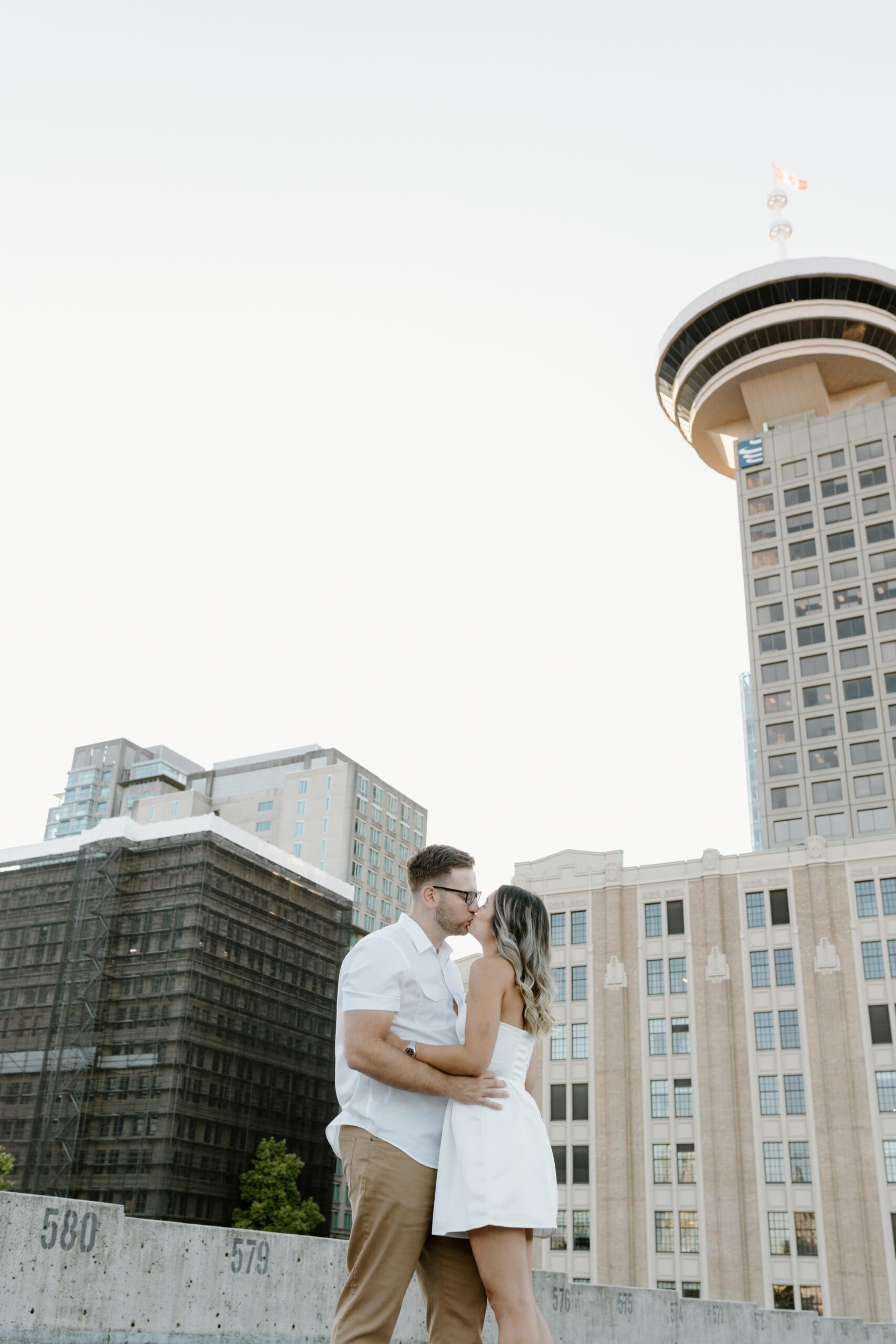 Editorial image of a man and woman kissing on a rooftop in Vancouver, surrounded by tall building